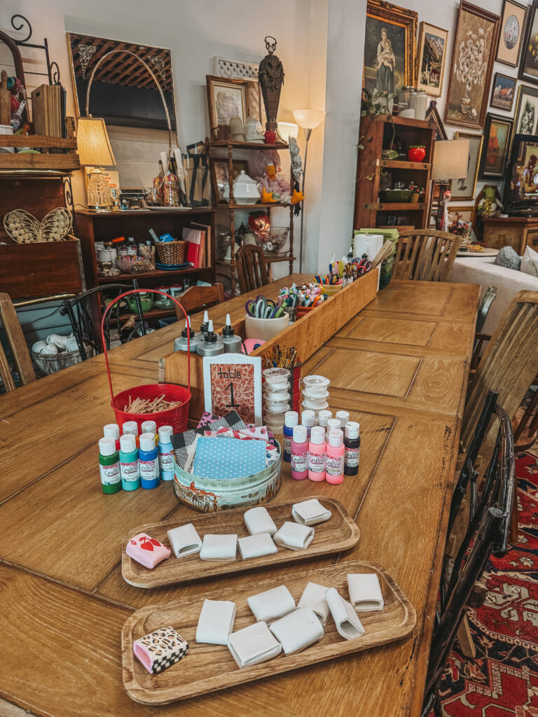 craft station setup for decorating clay matchbox covers with paints, brushes, and supplies at a women's DIY workshop