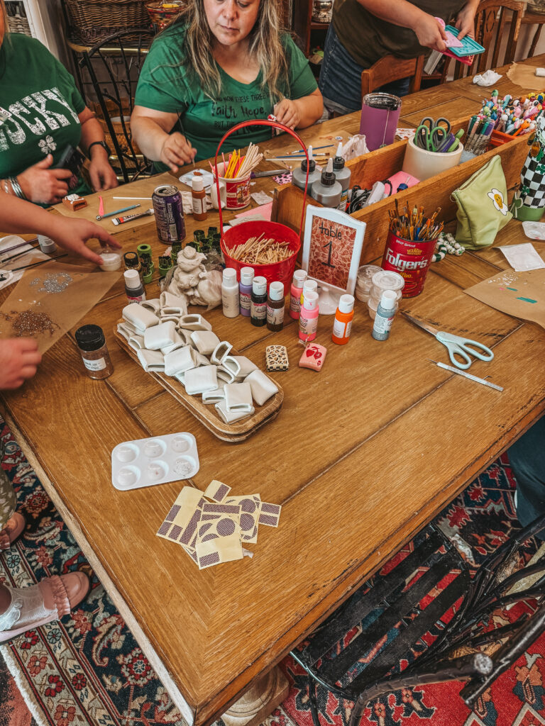 women painting and decorating clay matchbox covers at a diy craft workshop with paintbrushes, and supplies on a wooden table