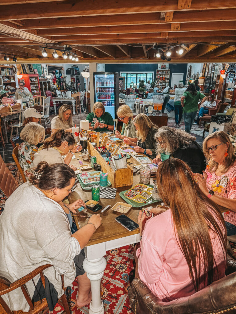 A large group of smiling women at a "Granny Camp" retreat posing together in a rustic living room proudly holding up their handmade miniature crafts.