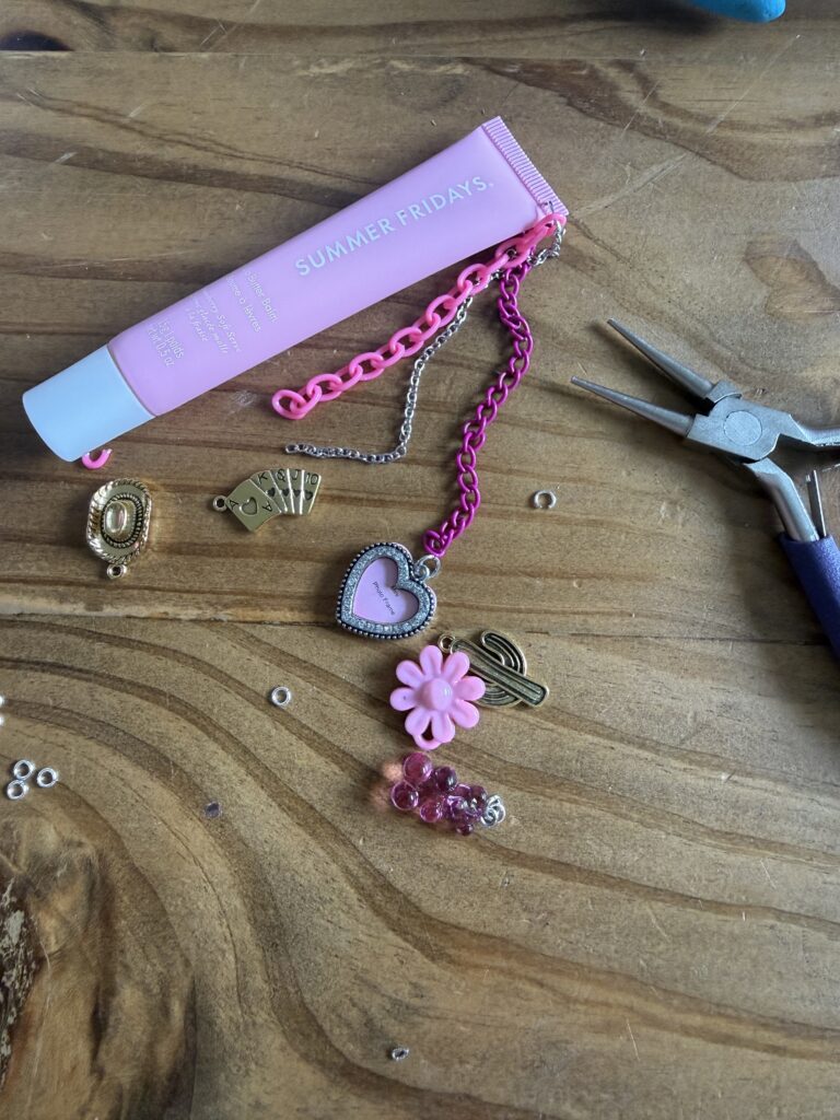 Step-by-step tutorial for DIY lip gloss charms featuring purple Summer Fridays balm, jewelry pliers, pink heart locket, and gold western charms on a wood table.