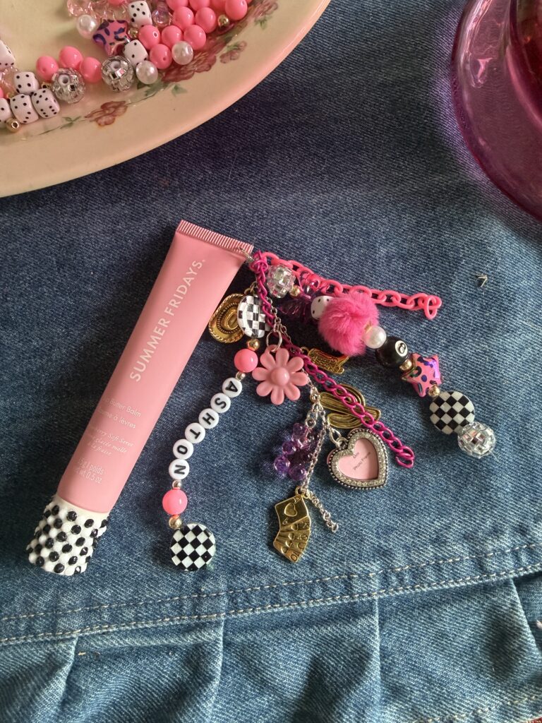 DIY lip gloss charm holder with personalized pink Summer Fridays butter balm, 'Ashton' name beads, and aesthetic charms on denim background