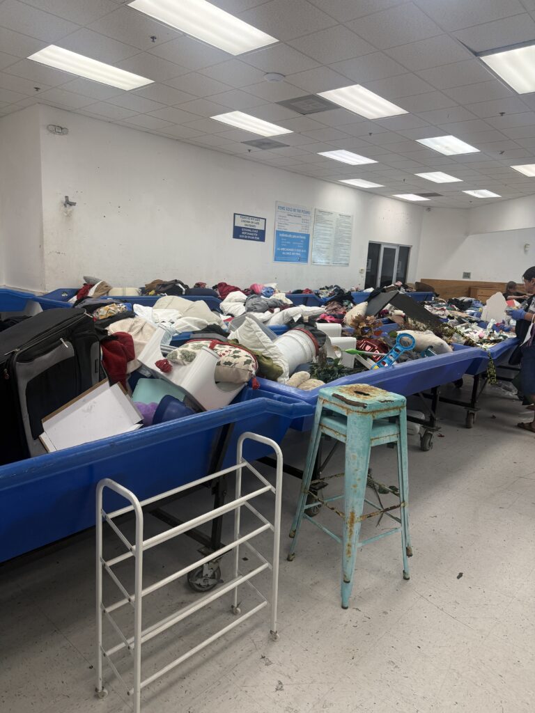 Houston Goodwill outlet bins filled with assorted clothing as shoppers search through large blue bins in a busy thrift store warehouse setting.