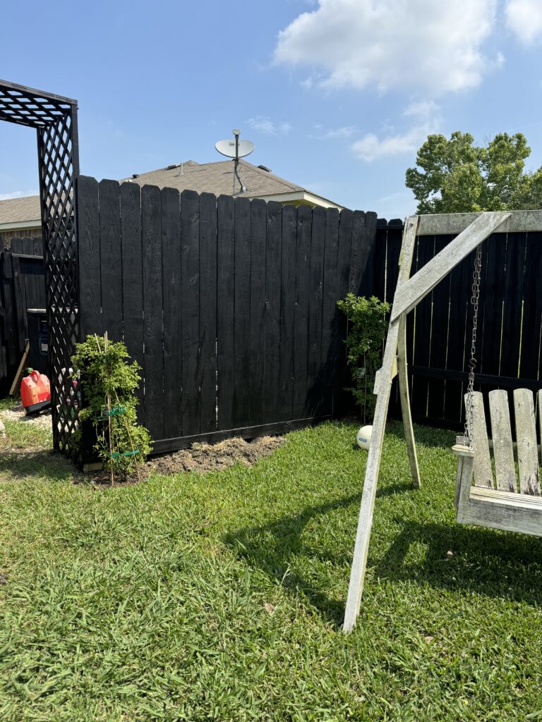  a weathered, graying wooden swing set against a dark painted fence.