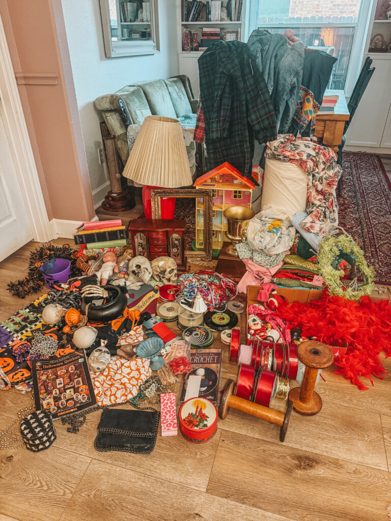 A colorful spread of vintage thrift finds arranged on a wooden floor, including ribbons, books, small decor pieces, and eclectic craft supplies from Houston Goodwill bins.