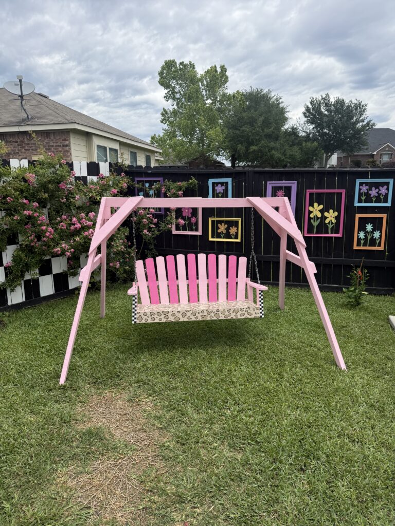 vibrant, "funky" aesthetic featuring a bright pink, cheetah painted swing set, a black and white checkered accent wall, and colorful floral artwork hanging on the fence.
