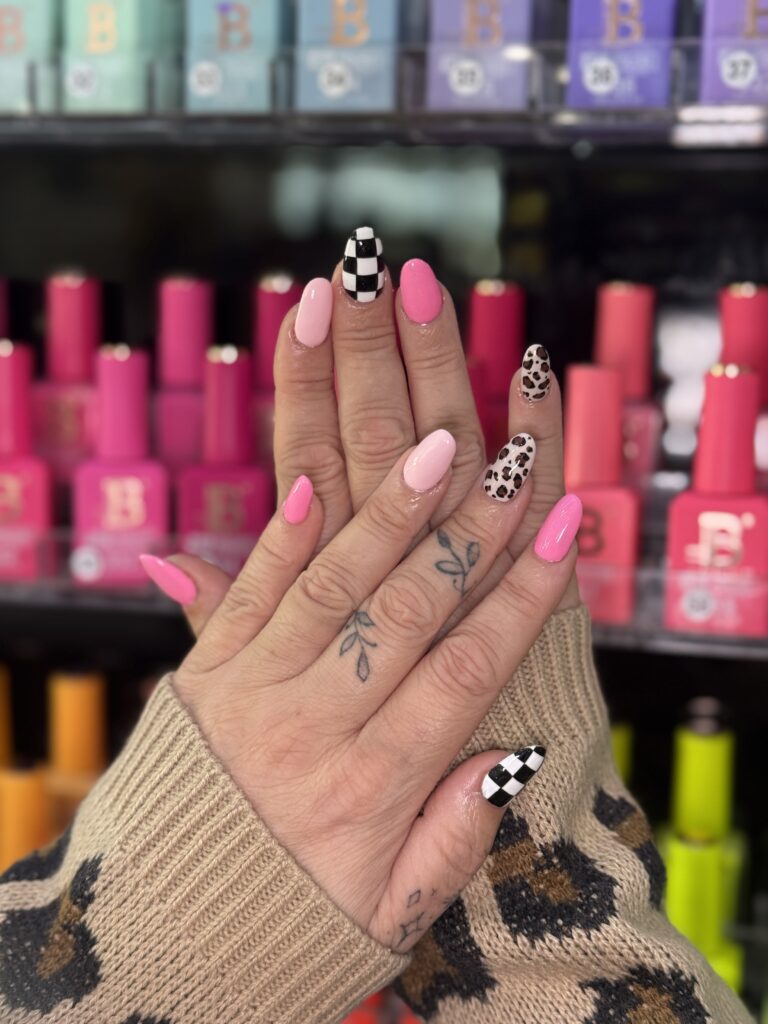 Close-up of almond-shaped nails painted with solid pink, checkerboard, and leopard print designs.