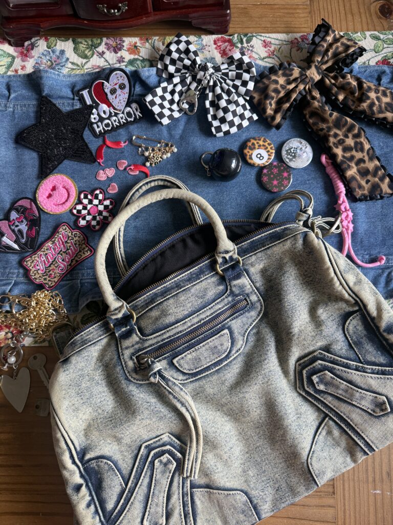 Flat lay of DIY craft supplies including patches, bows, and beads surrounding a plain denim handbag.