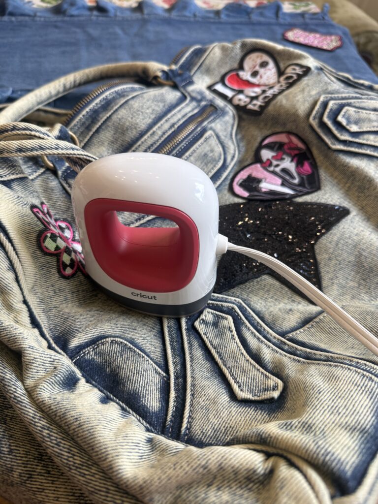 Mini Cricut EasyPress sitting on a denim bag next to iron-on patches being applied.