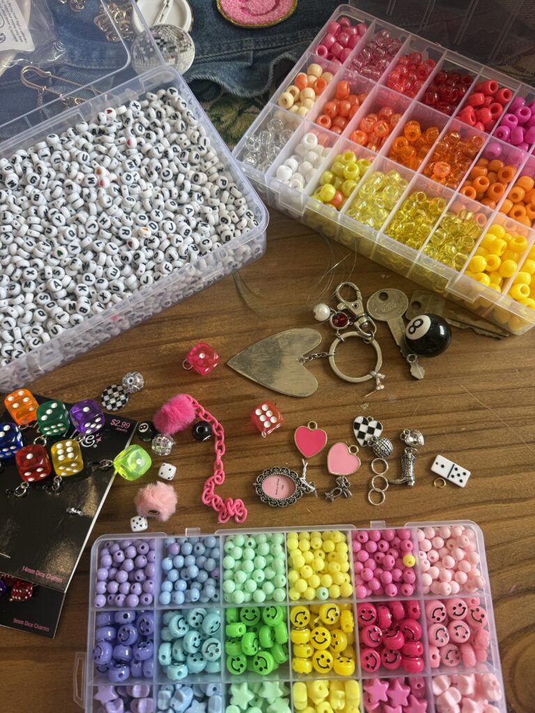 Crafting supplies including bead organizers, colorful dice, and metal charms for making bag accessories.
