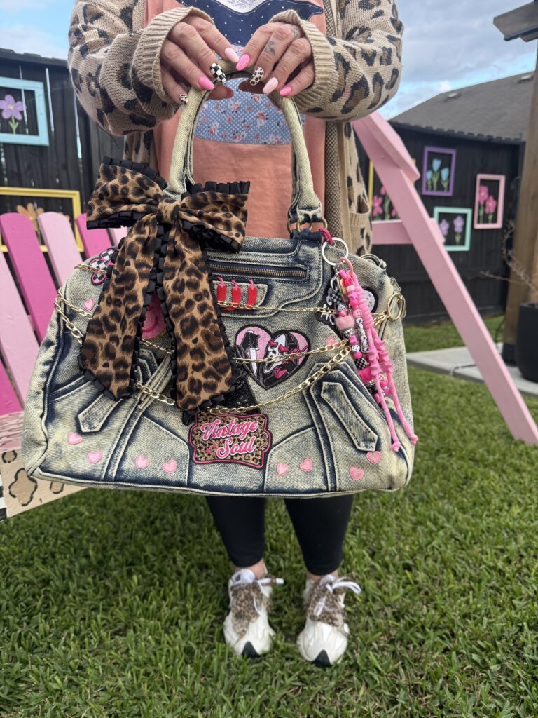 Person holding a custom Y2K junk purse made from denim, decorated with a leopard bow, patches, and beaded charms.