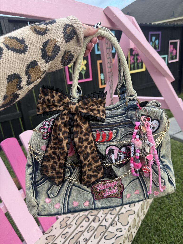 Close-up of a decorated Y2K denim junk purse featuring a large leopard print bow, chains, and iron-on patches.