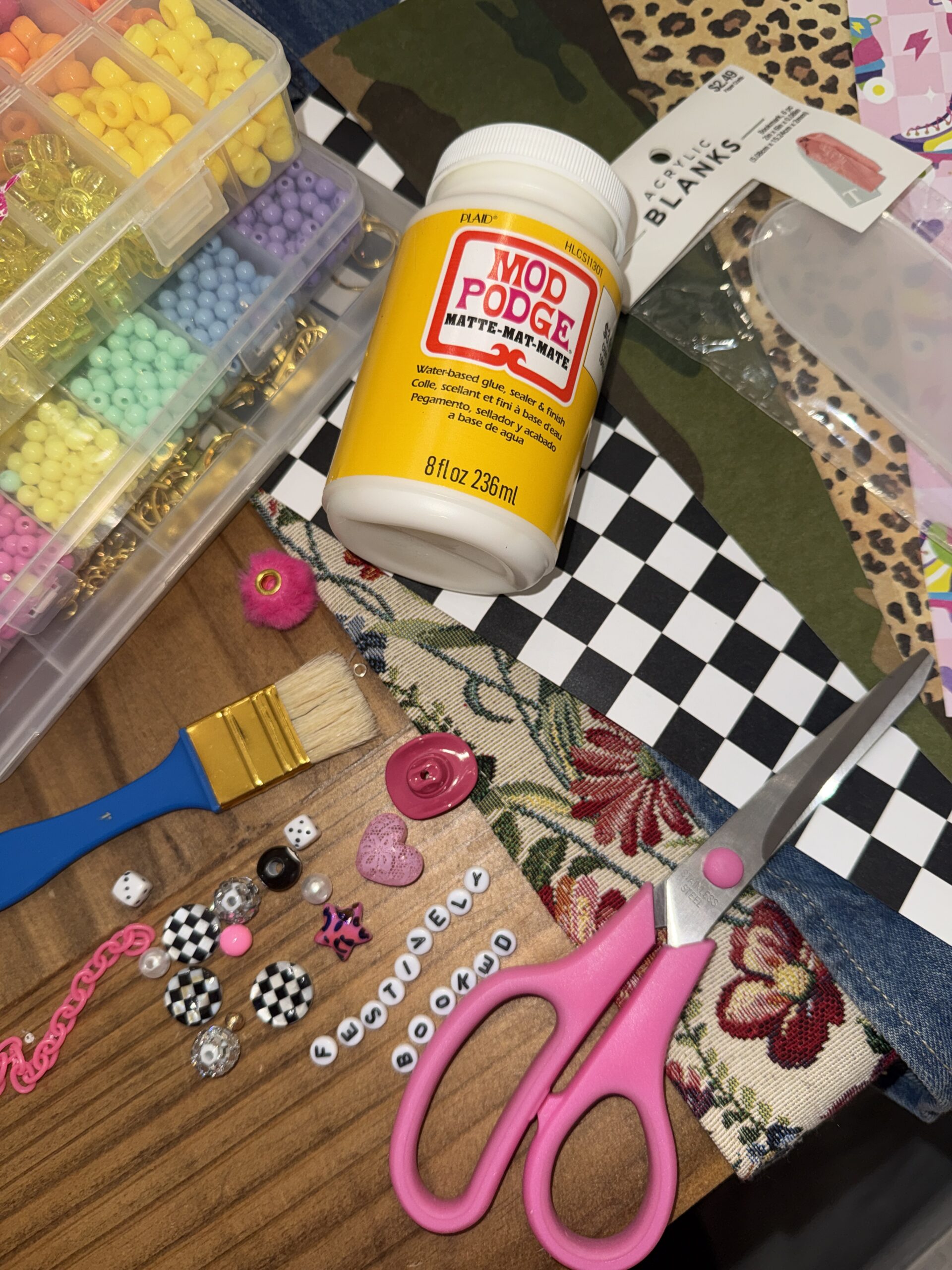 DIY junk bookmark materials featuring Mod Podge matte sealer, colorful plastic beads, and acrylic blanks for crafting.