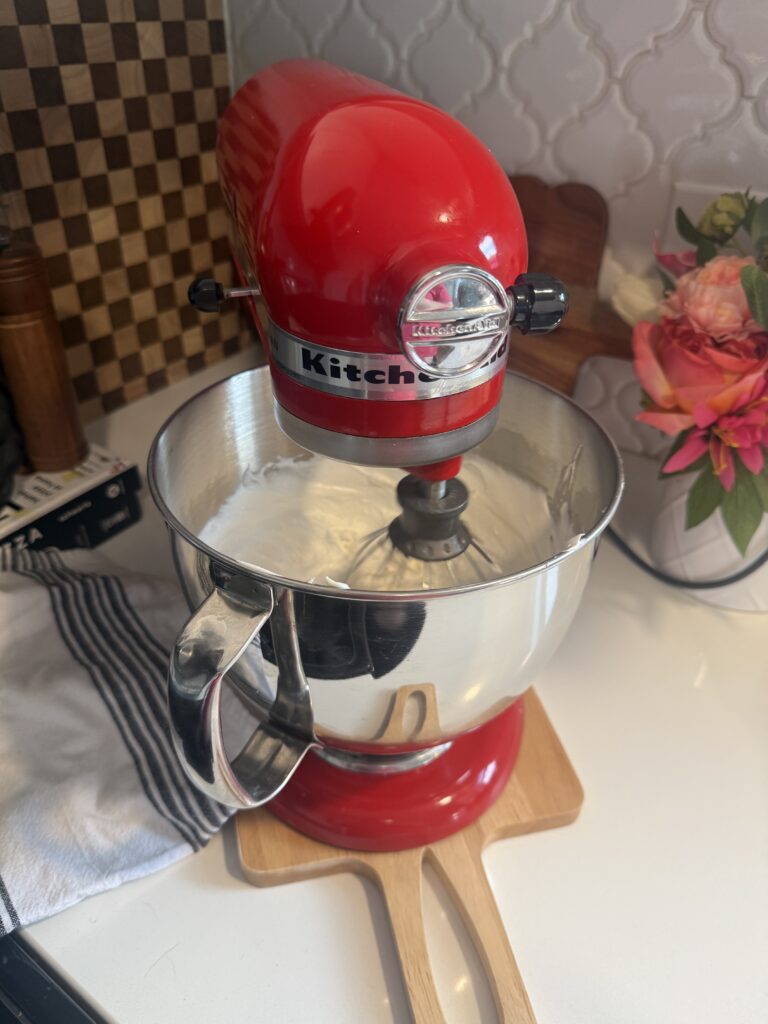 A red kitchenaid stand mixer whipping frosting.