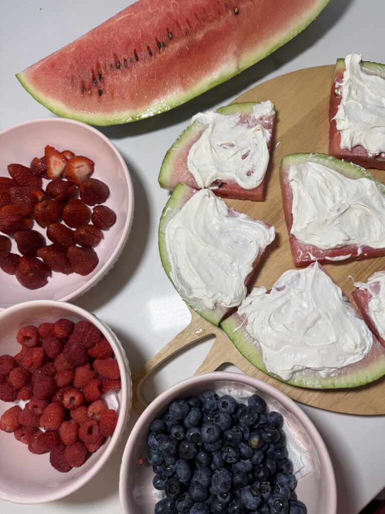 plain watermelon slices spread with white frosting alongside bowls of fresh berries ready for topping.